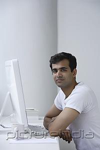 PictureIndia - Indian man working on computer, looking at camera.