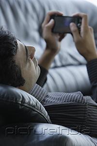 PictureIndia - Indian man laying on black sofa surfing on phone.