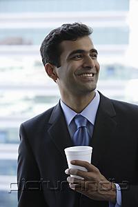 PictureIndia - Head shot of Indian businessman holding cup and smiling.