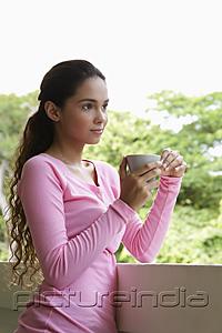 PictureIndia - Young woman holding cup leaning on balcony