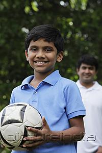 PictureIndia - Young boy holding ball while father stands behind him