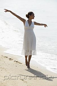 PictureIndia - young woman with arms out stretched walking along the beach