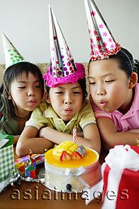 Asia Images Group - Three girls with party hats blowing candle on birthday cake