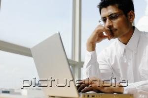 PictureIndia - Man using laptop, hand on chin