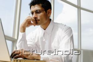 PictureIndia - Man using laptop, hand on chin, portrait