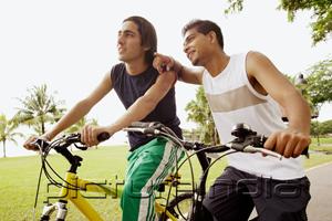 PictureIndia - Two young men on bicycles, one leaning on the other, pointing