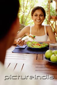 PictureIndia - Woman at table with plate of salad, looking at man across from her