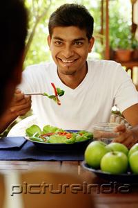 PictureIndia - Man eating salad, looking at person opposite him