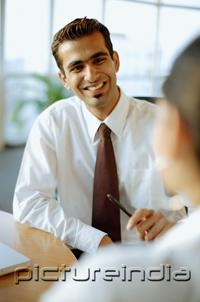 PictureIndia - Male executive smiling at person in front of him, over the shoulder view