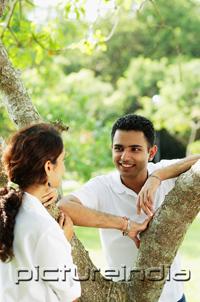 PictureIndia - Couple looking at each other, standing on either side of tree