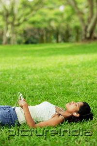PictureIndia - Young woman listening to music with headphones, lying on grass