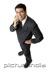 PictureIndia - Businessman, using mobile phone, looking at camera, hand on hip