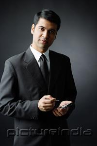 PictureIndia - Businessman looking at camera, holding PDA
