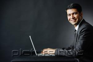 PictureIndia - Businessman smiling at camera, using laptop