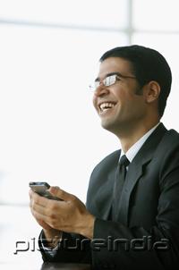 PictureIndia - Businessman holding PDA, smiling, looking away