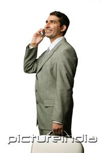 PictureIndia - Businessman using mobile phone, carrying briefcase, smiling