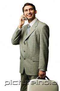PictureIndia - Businessman using mobile phone, carrying briefcase, looking away
