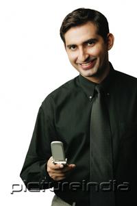 PictureIndia - Executive holding mobile phone, smiling at camera