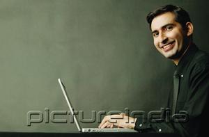 PictureIndia - Man using laptop, smiling at camera