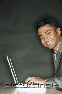 PictureIndia - Businessman using laptop, smiling at camera