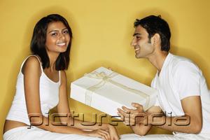 PictureIndia - Couple sitting face to face, woman looking at camera, man holding gift