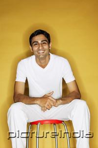 PictureIndia - Young man sitting on stool, looking at camera