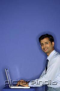 PictureIndia - Man using laptop, smiling at camera, portrait