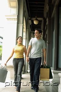 PictureIndia - Young man and woman walking, holding hands and carrying shopping bags