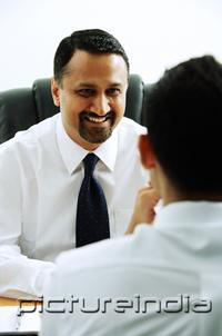 PictureIndia - Two businessmen in office, talking face to face, over the shoulder view