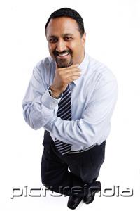 PictureIndia - Businessman looking up at camera, arms crossed, hand on chin
