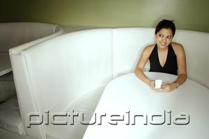 PictureIndia - Young woman sitting in booth holding mobile phone, looking away