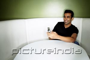 PictureIndia - Young man sitting in booth, looking at mobile phone