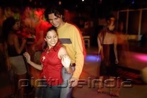 PictureIndia - Young adults dancing in night club, couple in the foreground