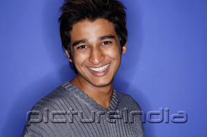 PictureIndia - Man against blue background, smiling at camera