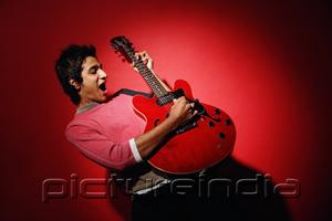 PictureIndia - Young man playing guitar, standing against red wall