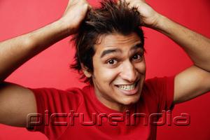 PictureIndia - Man in red T-shirt against red background, pulling hair