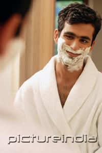 PictureIndia - Man looking in mirror having cream on face