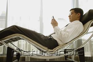 PictureIndia - Businessman reclining on chair, using PDA
