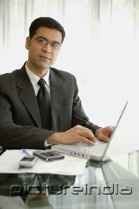 PictureIndia - Businessman sitting at desk with laptop, PDA and mobile phone