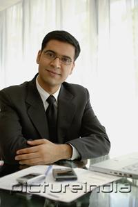 PictureIndia - Businessman sitting at desk with laptop, PDA and mobile phone, looking at camera