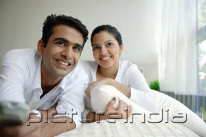 PictureIndia - Couple lying on bed, man holding remote control