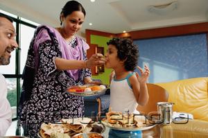 PictureIndia - Family of three having a meal at home, mother feeding daughter