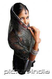 PictureIndia - Woman in gray sari standing against white background, shielding face scarf