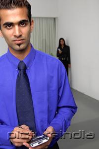 PictureIndia - Businessman holding PDA, woman in the background