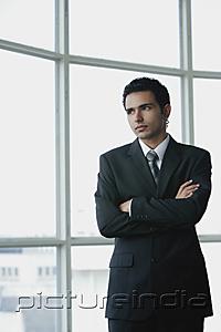 PictureIndia - Young businessman arms crossed, standing by window