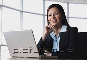 PictureIndia - Businesswoman sitting in front of laptop, hand on chin, smiling