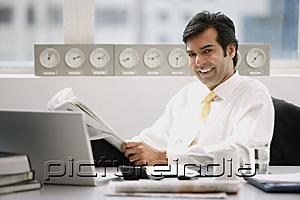 PictureIndia - Businessman sitting in office, holding newspaper, smiling