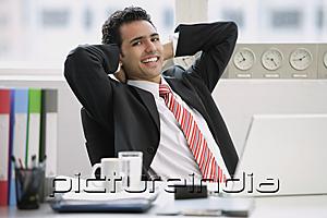 PictureIndia - Businessman sitting in office, hands behind head, smiling at camera
