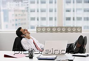 PictureIndia - Businessman in office, using mobile phone, feet up on desk