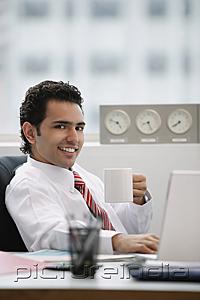 PictureIndia - Businessman in office, holding coffee mug, smiling